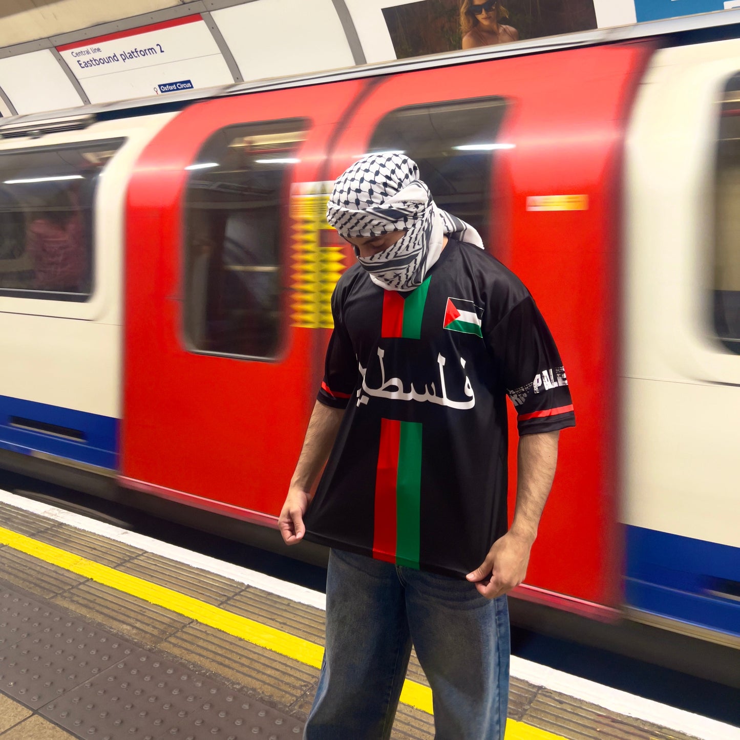 Person wearing a headscarf and black P4L Palestine jersey in front of a moving train.
